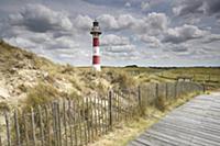 Raised wooden walkway through dunes beside lightho