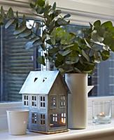 House lantern next to vase of leaves on windowsill