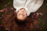 Girl with long auburn hair lying on grass amongst 
