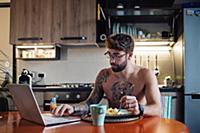 Mid adult man with tattoos eating omelette while t