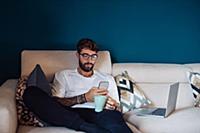 Mid adult man reclining on sofa looking at smartph