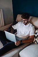 Mid adult man reclining on sofa using laptop