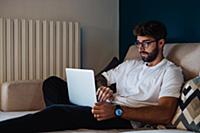 Mid adult man sitting on sofa typing on laptop