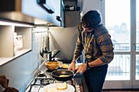 Mid adult man preparing fried eggs at kitchen hob 