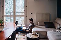 Mid adult man sitting on living room floor using l