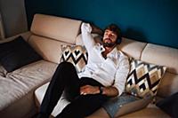 Mid adult man reclining on sofa listening to headp