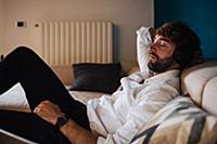 Mid adult man reclining on sofa listening to headp