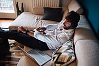 Mid adult man reclining on sofa listening to headp