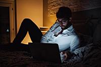 Mid adult man reclining on bed using laptop at nig
