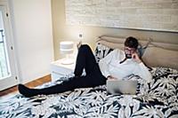 Mid adult man reclining on bed using laptop