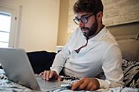 Mid adult man reclining on bed looking at laptop