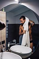 Mid adult man with tattoos drying hair at bathroom