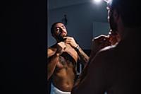 Mid adult man with tattoos trimming beard at bathr
