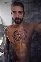Mid adult man with tattooed chest in shower, portr