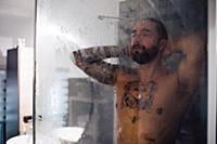 Mid adult man with tattooed chest taking a shower 