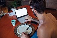 Mid adult man typing on laptop at breakfast table