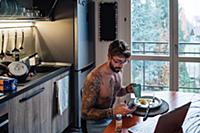 Mid adult man with tattoos drinking coffee while l