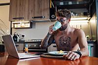 Mid adult man with tattoos drinking coffee while l