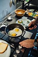 Mid adult man preparing fried eggs at kitchen hob,