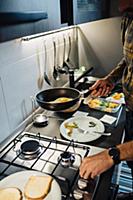 Mid adult man preparing fried eggs at kitchen hob,