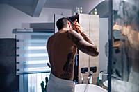 Mid adult man with tattoos combing hair at bathroo