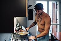 Mid adult man with tattooed chest using gas hob