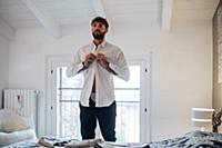Mid adult man fastening shirt in bedroom