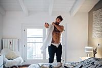 Mid adult man with tattoos putting on shirt in bed
