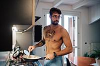 Mid adult man with tattoos cooking breakfast in fr
