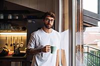 Mid adult man with coffee by apartment window, por