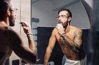 Mid adult man with tattoos brushing teeth at bathr
