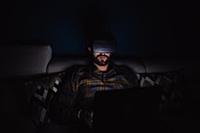 Bearded mid adult man sitting on sofa in darkness 
