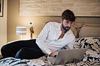 Mid adult man reclining on bed looking at laptop