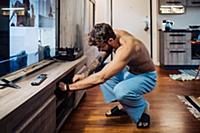Mid adult man crouching to open living room cupboa
