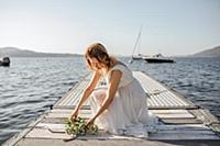 Young bride in wedding dress laying bouquet on lak