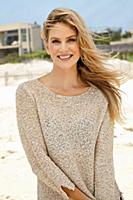 A young blonde woman on a beach wearing a beige kn