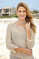 A young blonde woman on a beach wearing a beige kn