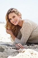 A young blonde woman lying on a beach wearing a be