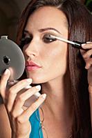 A brunette woman holding a compact mirror and appl