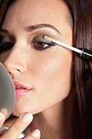 A brunette woman holding a compact mirror and appl