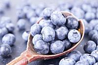 Old wooden spoonful of blueberries over on deep bl