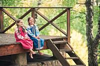 Девочки в русской народной одежде сидят на крыльце
